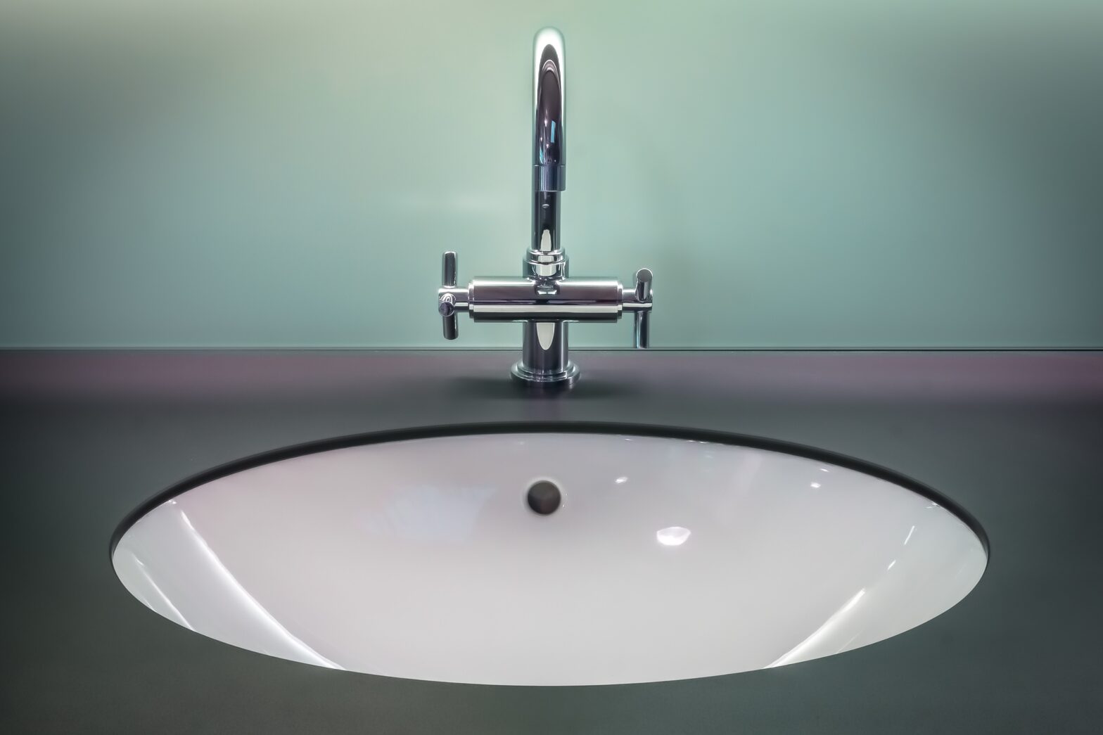 A close up image of a white inset sink with a teal glass splashback