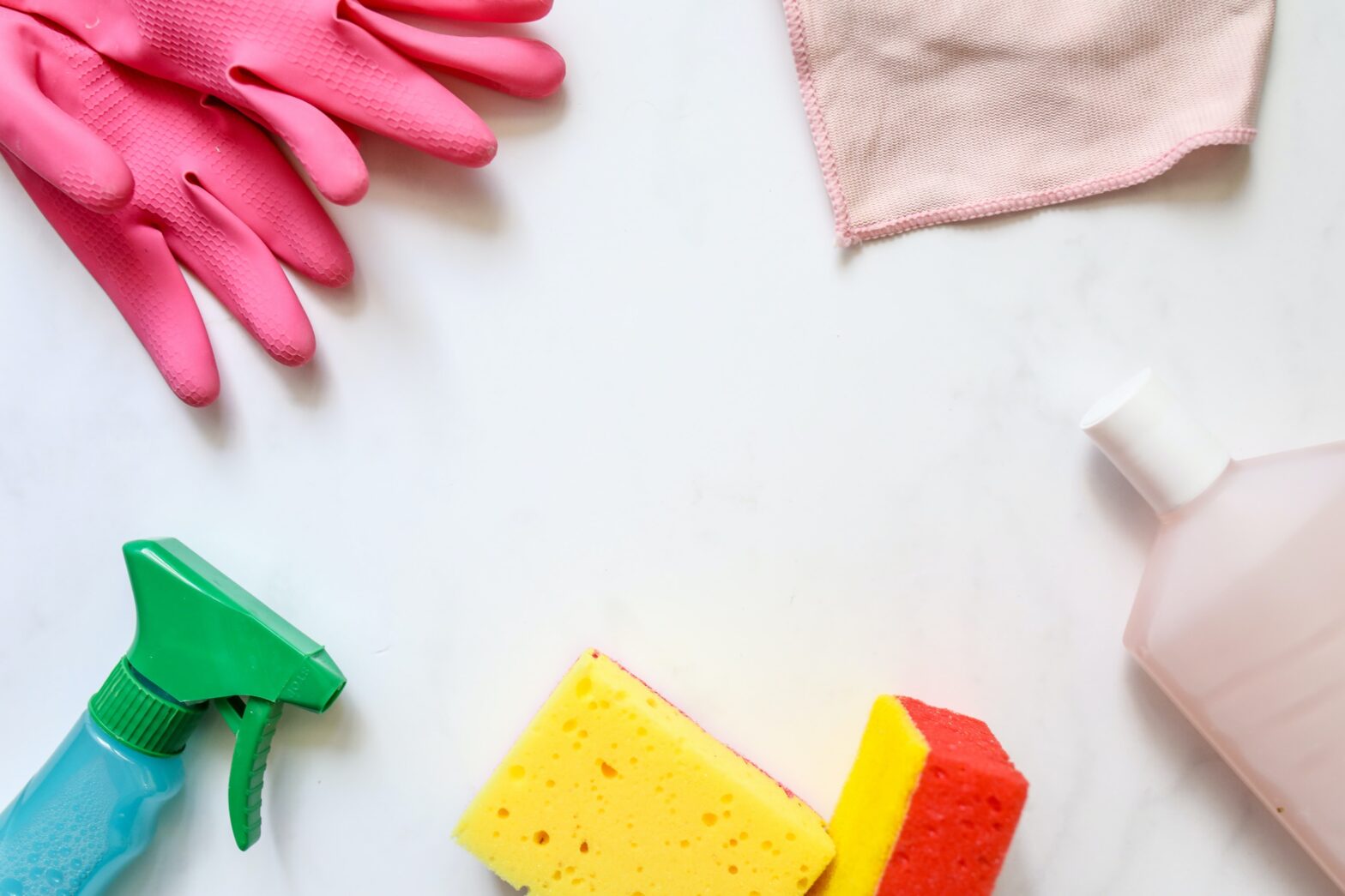 A pile of cleaning products, pink rubber gloves, yellow sponges, blue spray bottle