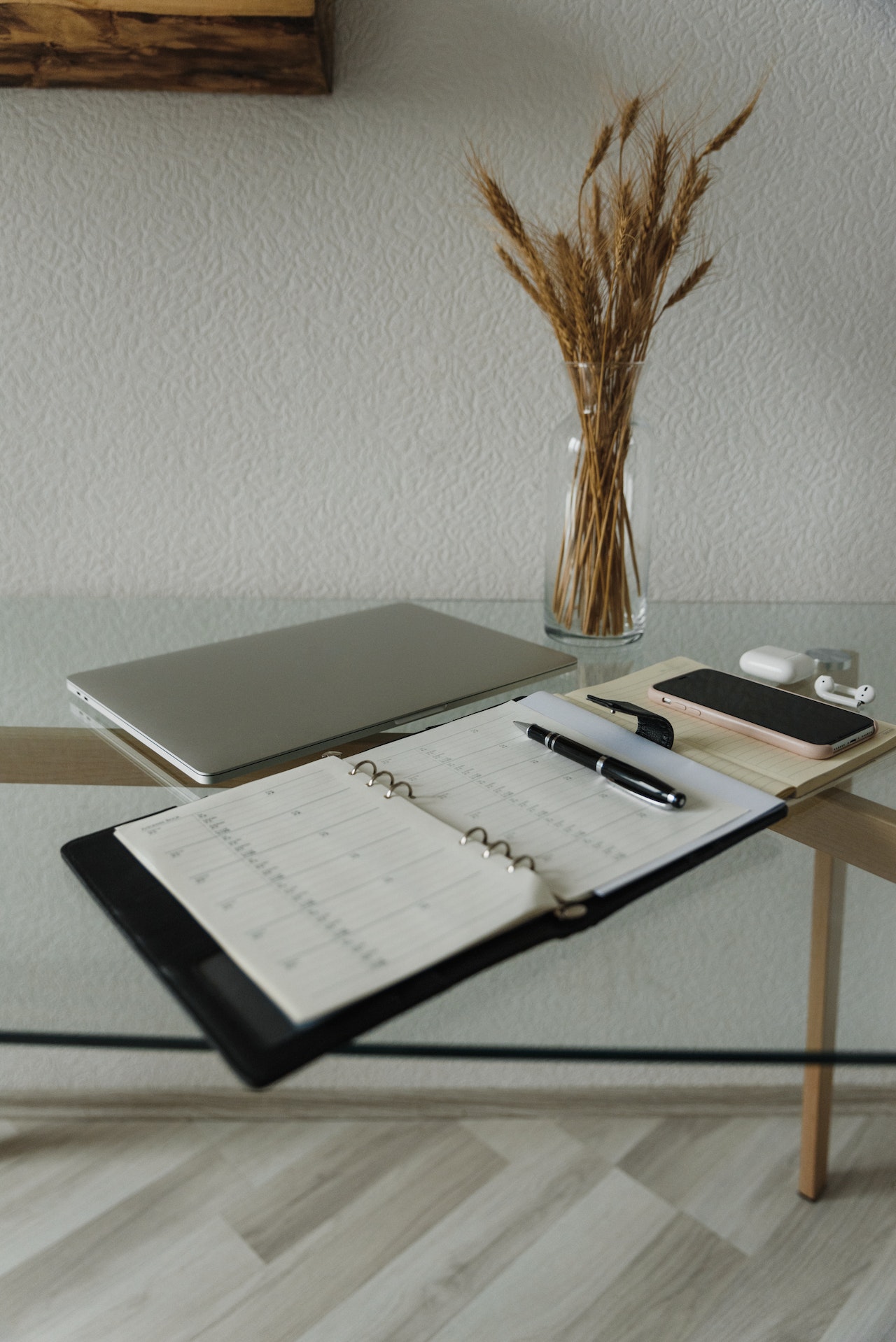 A notepad lays open on a glass table. There is also a macbook, phone, pens.